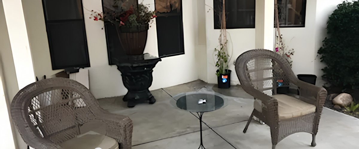 A cozy patio setup featuring a small glass table, comfortable chairs, and decorative plants.