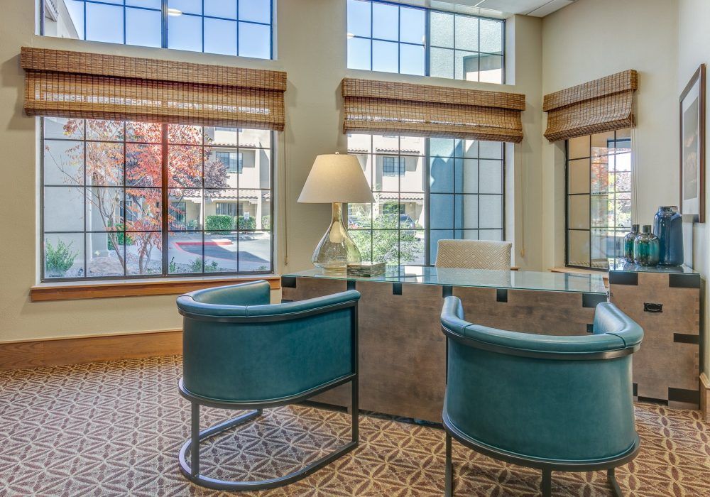 A modern office interior featuring a desk, two chairs, large windows, and a lamp.
