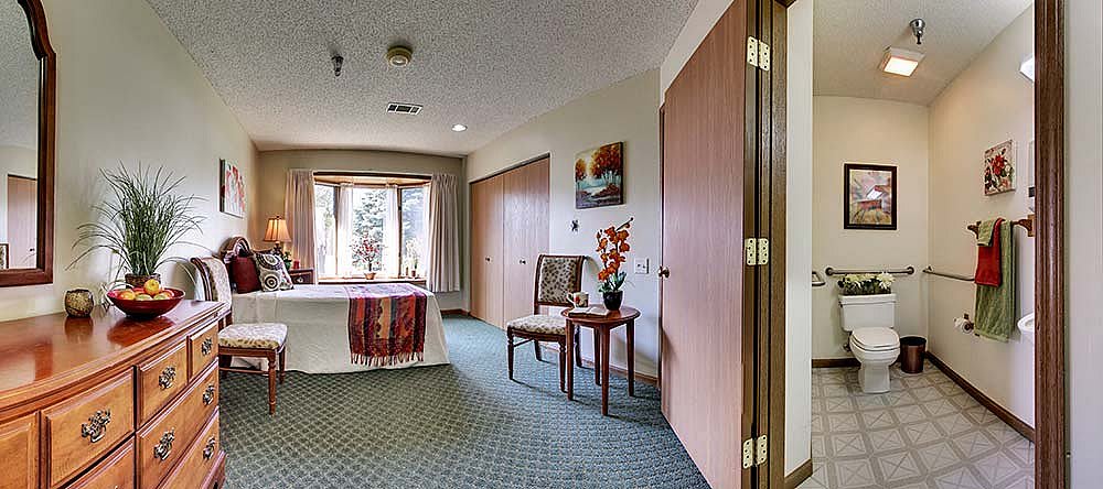 A cozy bedroom with a large window, carpeted floor, and simple decor.