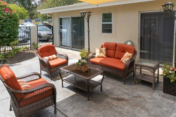A cozy outdoor seating area with orange-cushioned chairs and sofa arranged around a glass-top table on the patio.