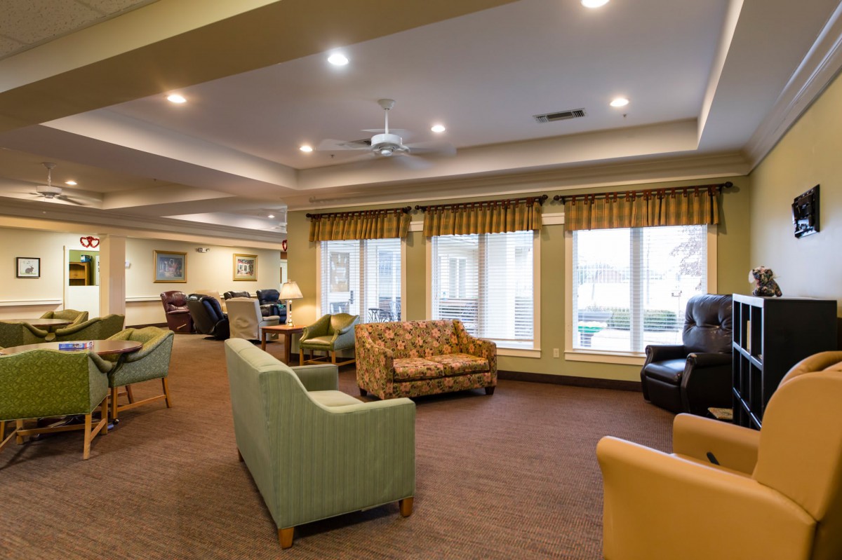 A cozy and spacious living room area with multiple sofas and armchairs, warmly lit with large windows.