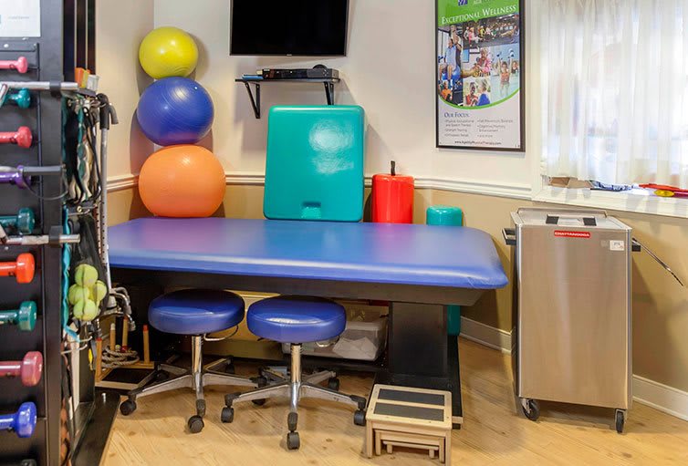 A physical therapy room featuring a treatment table, fitness balls, and exercise equipment.