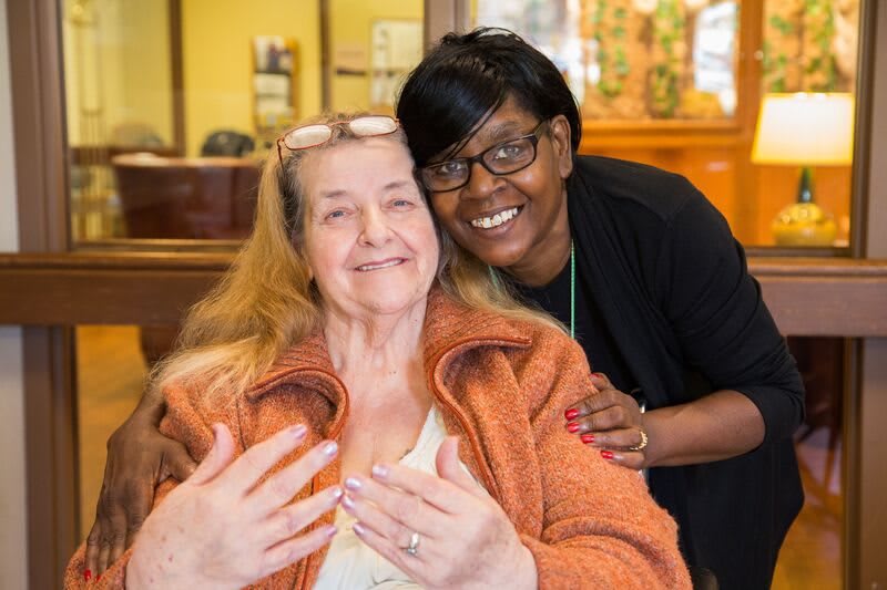 Two smiling people posing indoors, showing a bond of friendship.