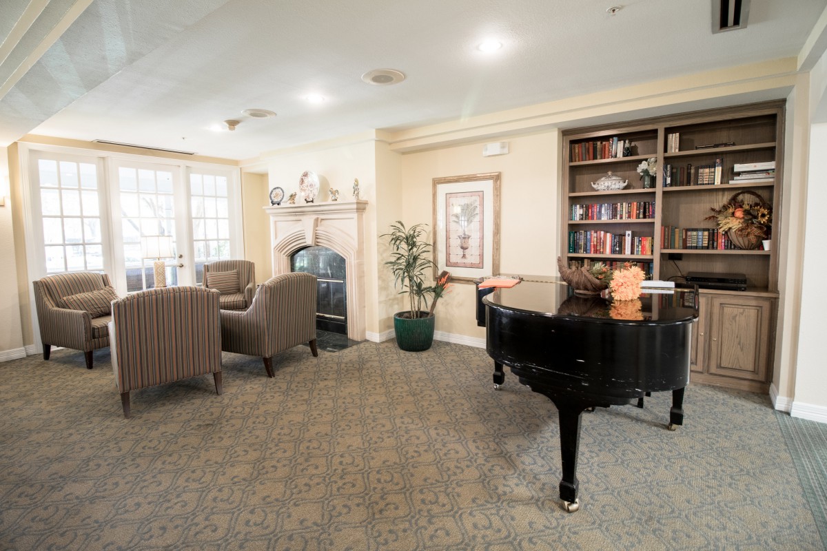 A cozy living room featuring a grand piano, bookshelf, and fireplace.