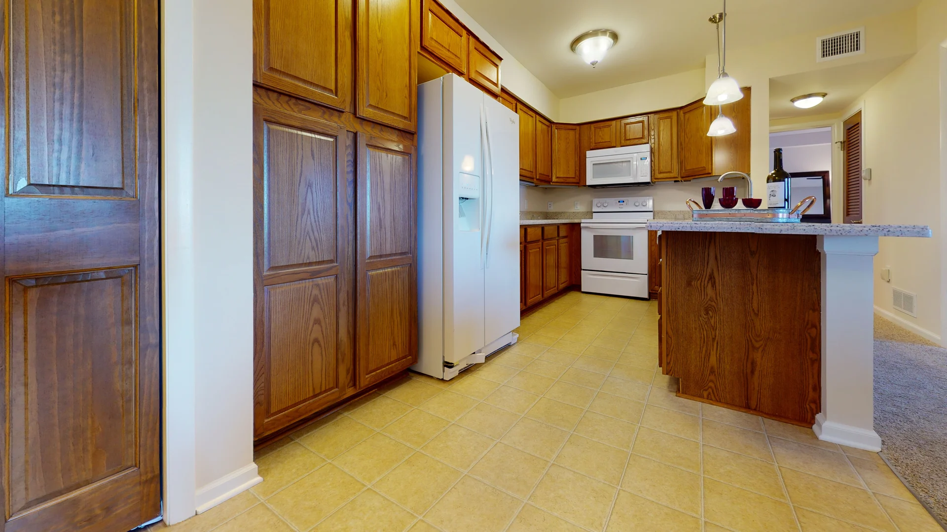 A spacious kitchen featuring wood cabinets, a white refrigerator, oven, microwave, and pendant lighting.