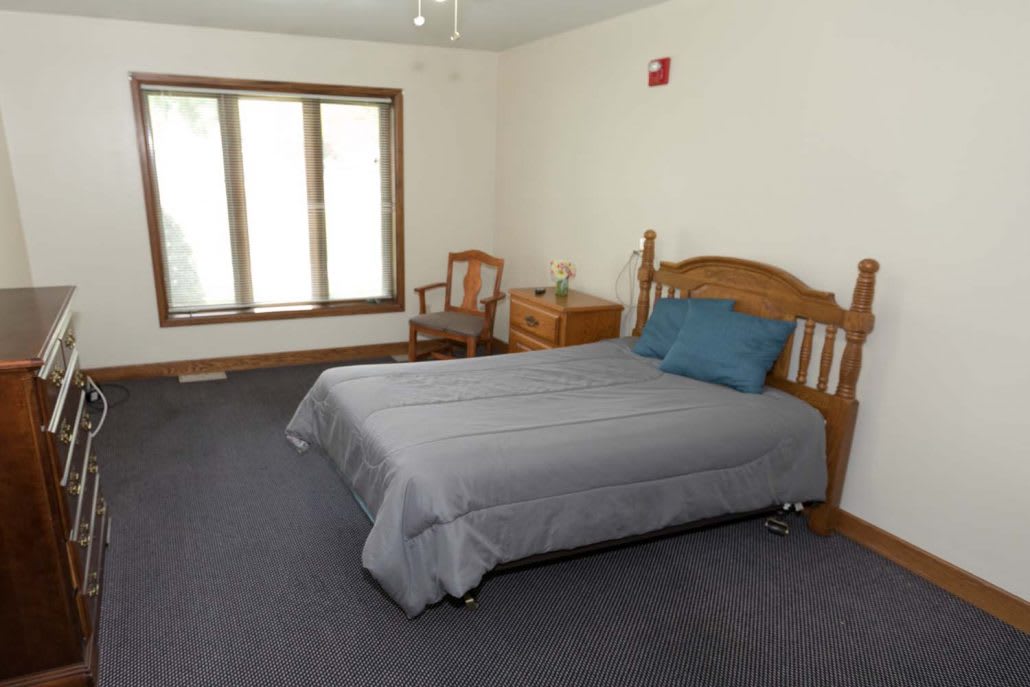 A minimalist bedroom with a bed, chair, and large window.