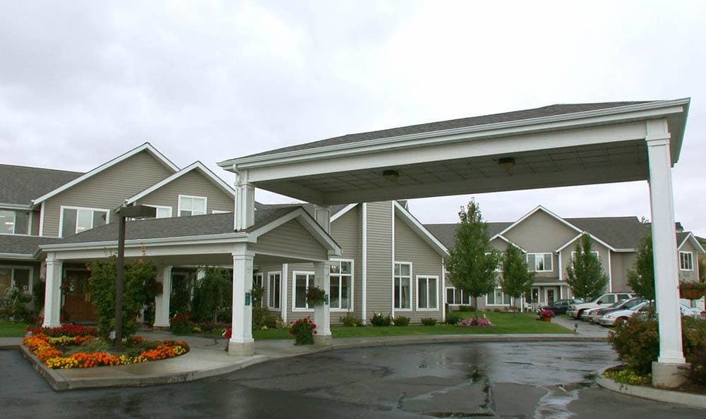 A modern building with a covered driveway entrance and landscaped surroundings on an overcast day.