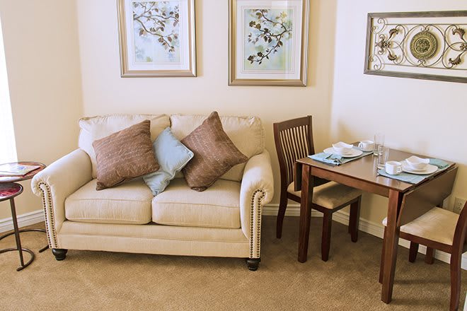 A cozy living room with a beige sofa adorned with cushions, accompanied by wall art and a small dining table.