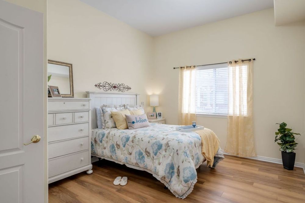 A cozy bedroom with light-colored walls, a bed with floral bedding, and a white dresser.