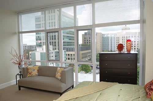 A modern apartment with large windows offering a cityscape view, featuring contemporary furniture and abundant natural light.