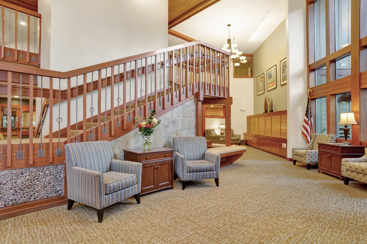 A cozy lobby area with two striped armchairs, a side table adorned with flowers, and a wooden staircase.