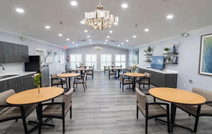 A modern dining area with elegantly arranged tables and chairs, featuring a central chandelier and bright lighting.
