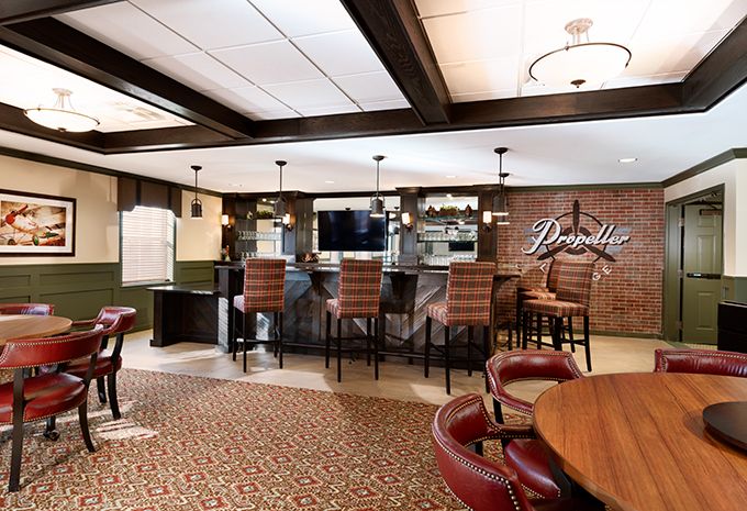A cozy bar lounge with comfortable seating and a television, featuring modern lighting and a patterned carpet.