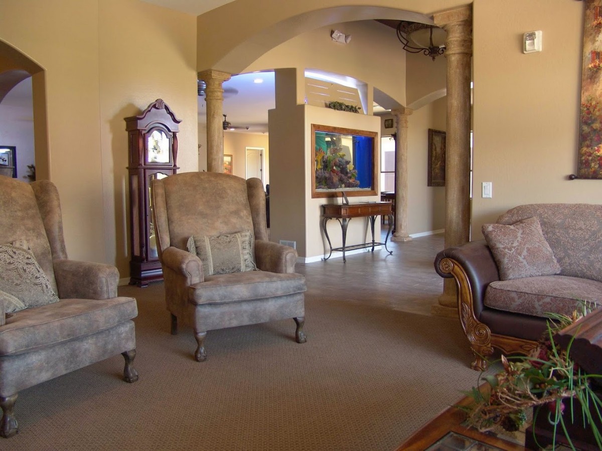 A cozy living room featuring elegant armchairs, a classic sofa, and a grandfather clock, with an open archway leading to another area.
