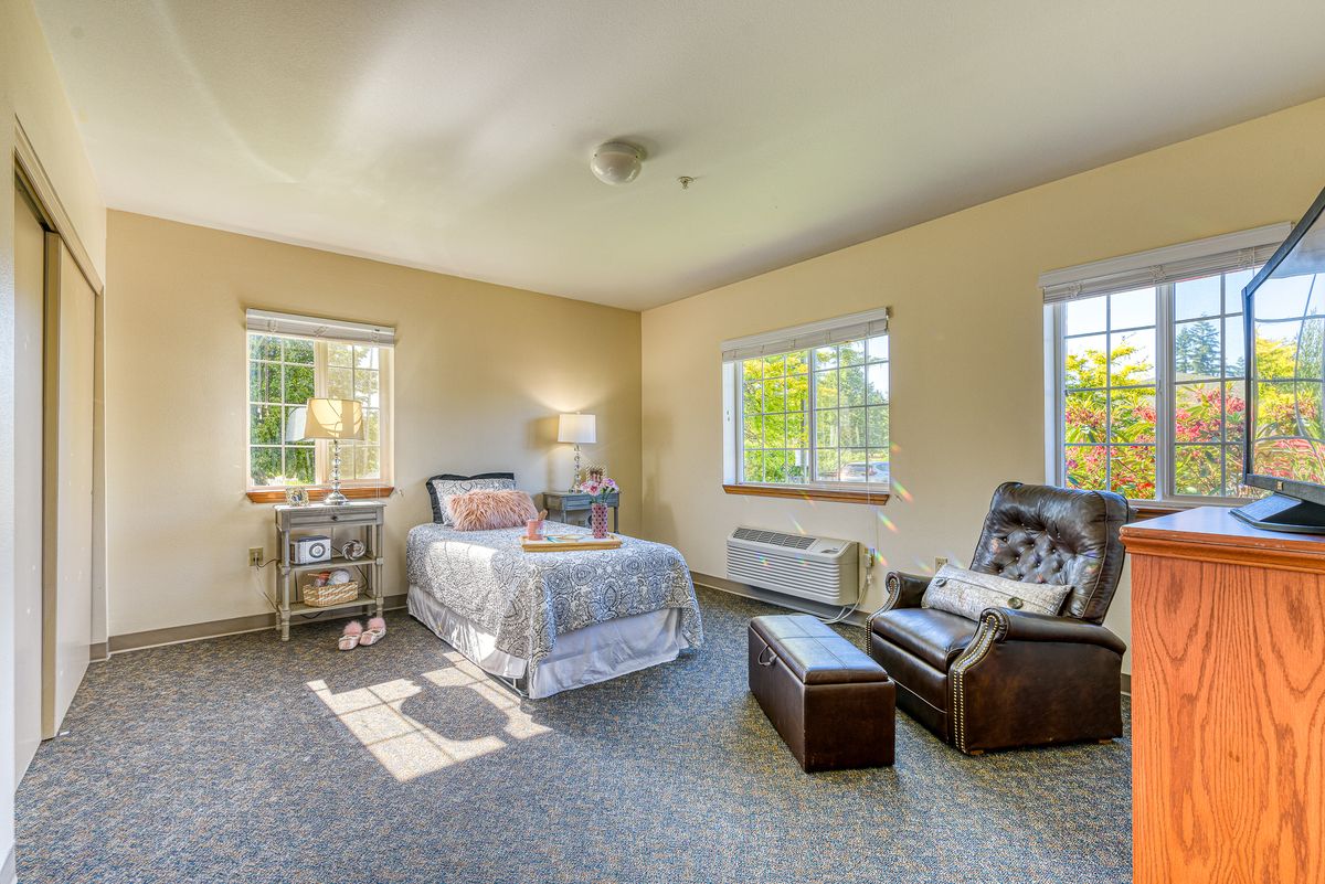 A cozy bedroom with a single bed, armchair, and natural light from large windows.