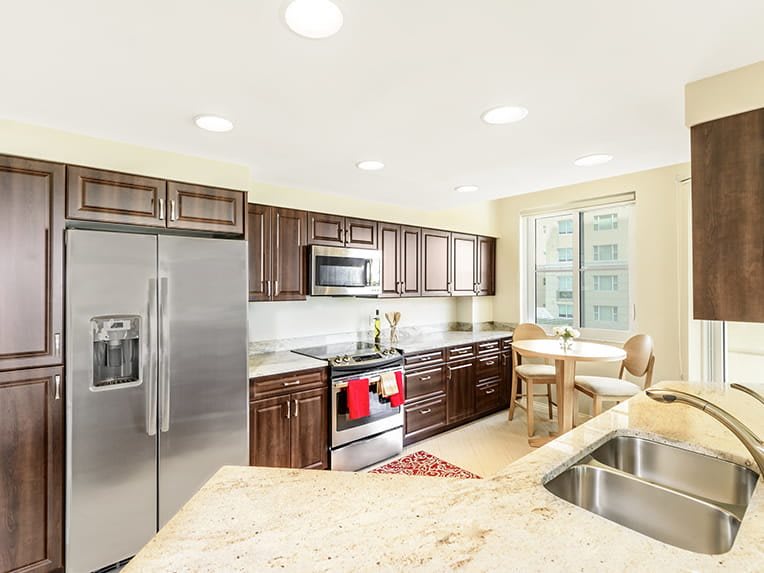 A modern kitchen with stainless steel appliances and wooden cabinets, featuring bright lighting and a window.
