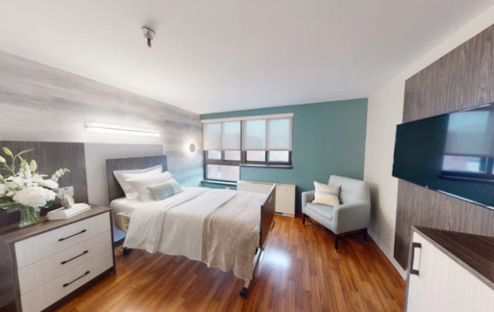 A modern and minimalist bedroom with a comfortable bed, an armchair, and large windows providing natural light.