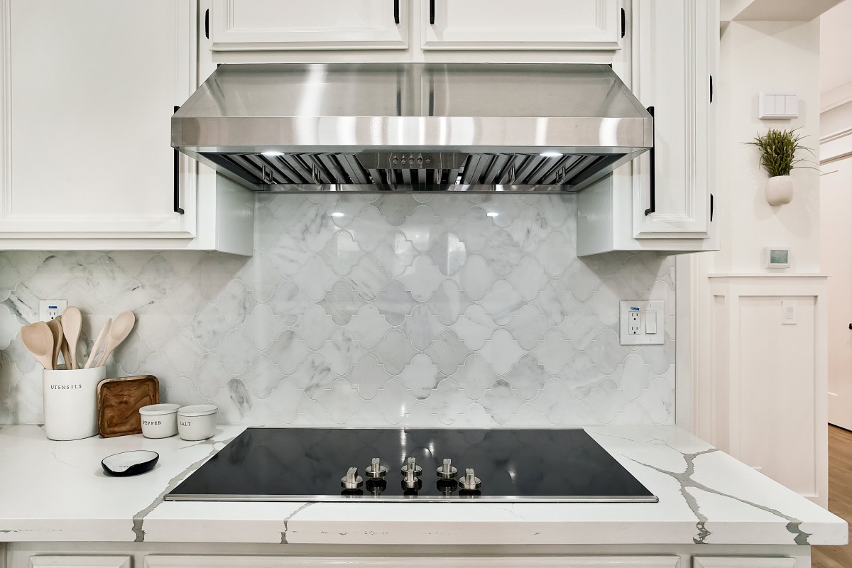 A modern kitchen with a sleek stovetop and stainless steel range hood, featuring a marble backsplash.