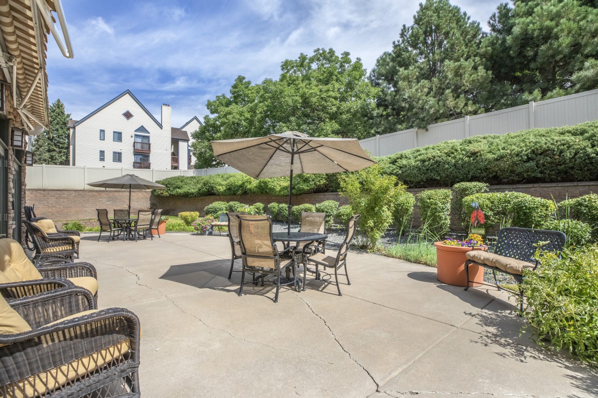 A sunny patio area with tables and chairs under umbrellas, surrounded by lush greenery.