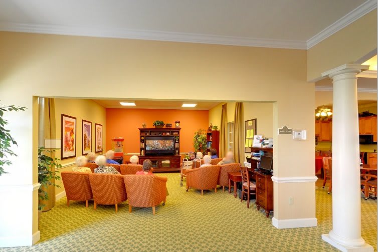 A common area in a senior living facility with chairs arranged around a television.