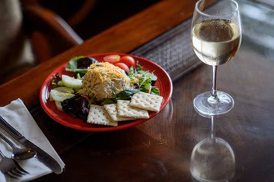 A gourmet meal with a fresh salad, cheese ball, crackers, and a glass of white wine.