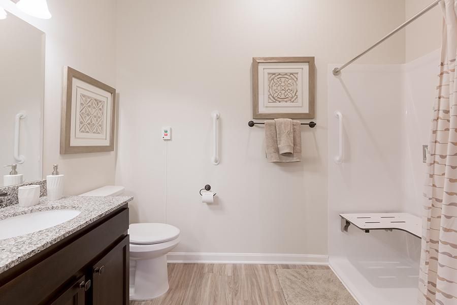 A clean and minimalist bathroom featuring a toilet, bathtub, towel rack, and framed artwork.