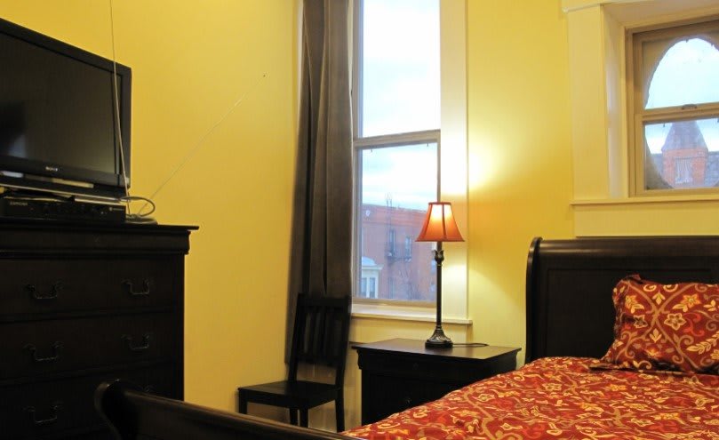 A cozy bedroom with a lamp on the nightstand by the window.