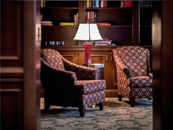 A cozy reading area with patterned armchairs and a lamp in a library setting.