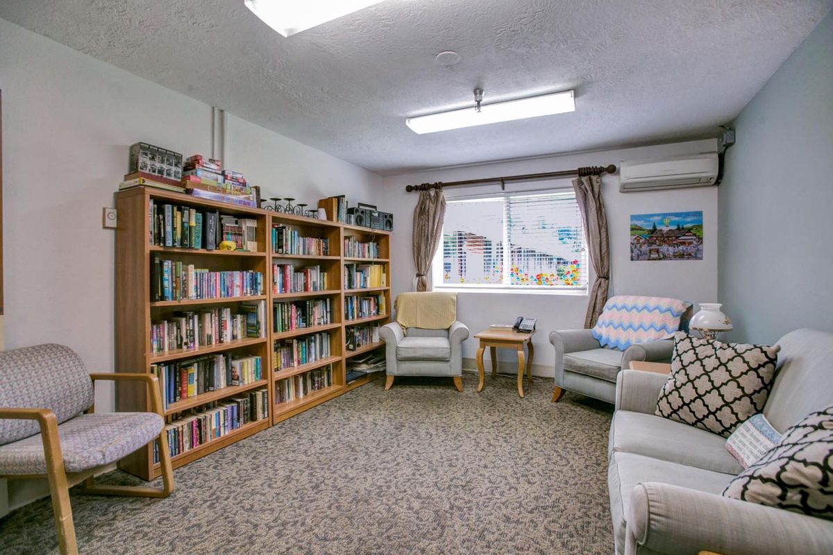 A cozy library room with bookshelves filled with books and comfortable armchairs by the window.