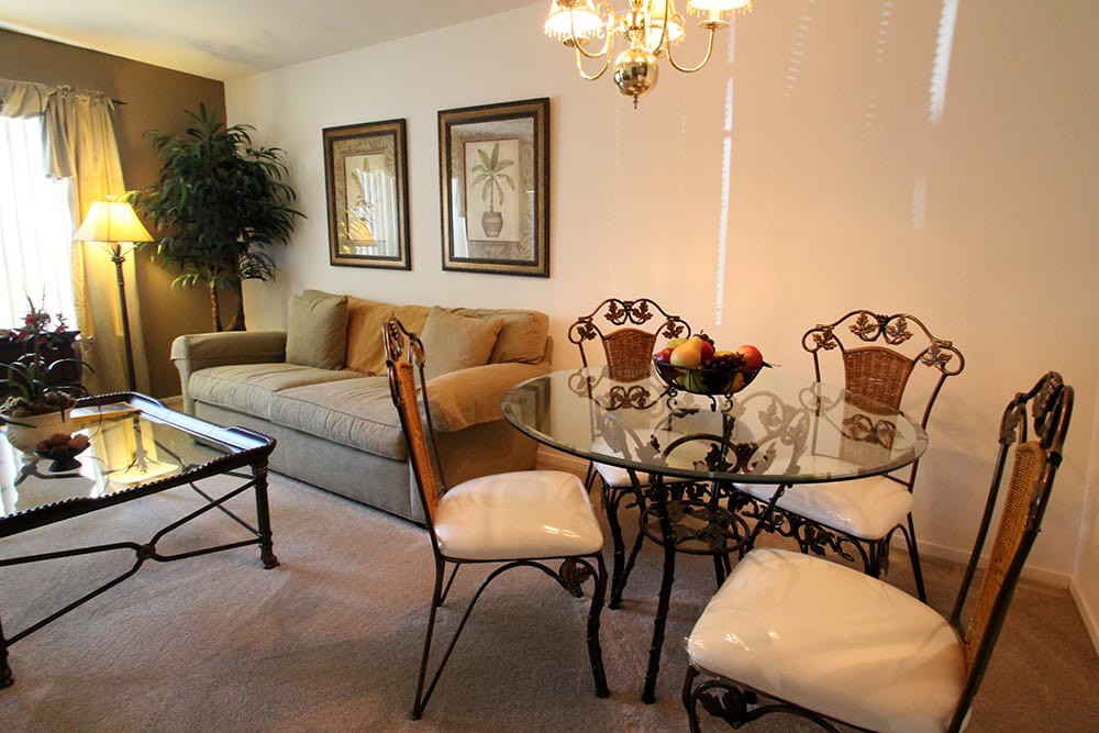 A cozy living room with a dining area featuring a glass table and upholstered chairs, complemented by elegant decor and wall art.