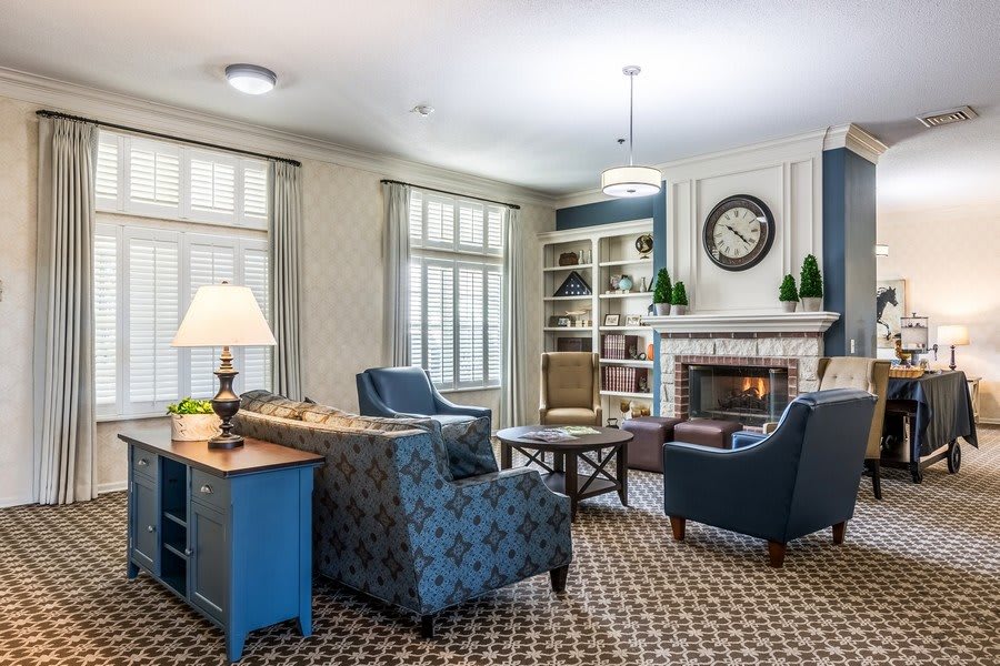 A cozy living room with comfortable seating around a fireplace, featuring elegant decor and a bookshelf.