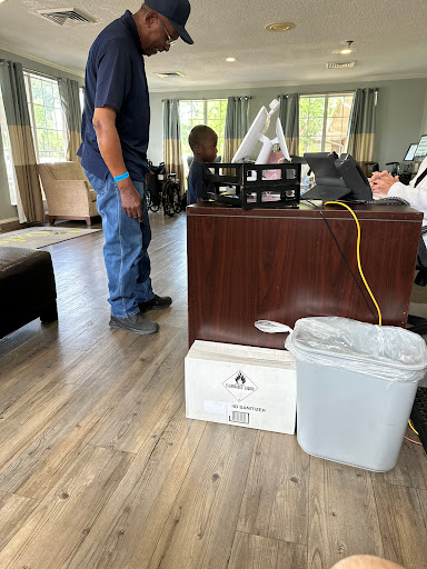 An indoor office setting featuring furniture, a person standing nearby, and a waste bin beside some boxes.