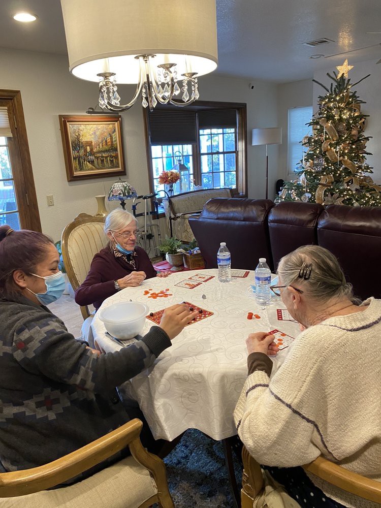 Elderly individuals enjoying a communal activity at a table near a decorated Christmas tree.