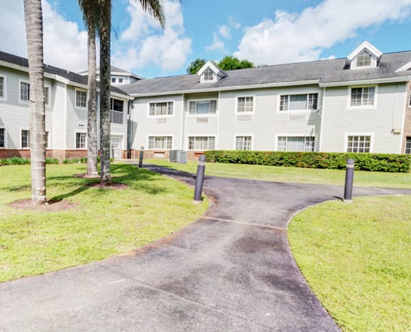 A pathway leading to a residential apartment complex surrounded by greenery and palm trees.