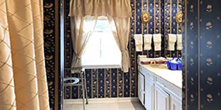 A retro kitchen featuring patterned wallpaper, a curtained window, and white cabinets.