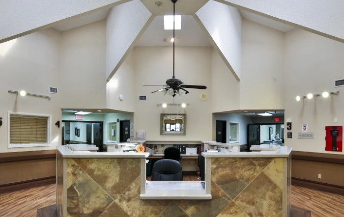 A spacious office reception area with a high ceiling, ceiling fan, and a central desk surrounded by marble flooring.