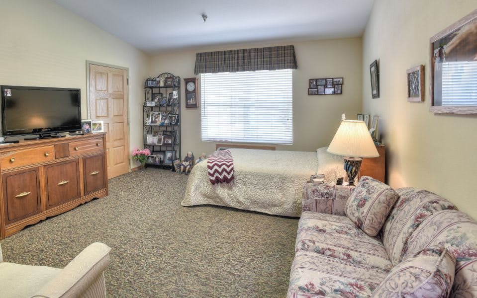 A cozy bedroom with a single bed, patterned sofa, and a well-lit window.