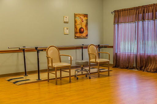 A spacious dance studio featuring two chairs, wooden flooring, and soft natural lighting.