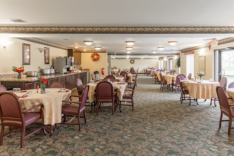 A spacious dining area with neatly arranged tables and chairs, featuring a buffet station and carpeted flooring.