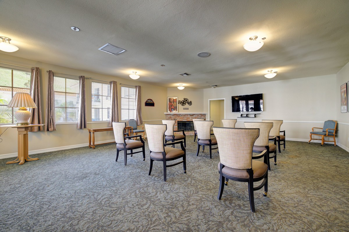 A spacious meeting room with chairs arranged around a central area, featuring large windows and a mounted television.