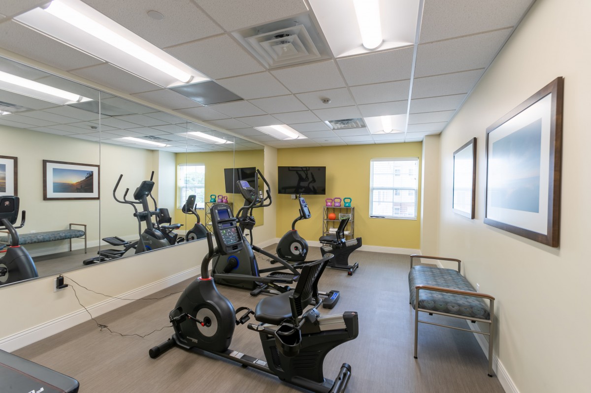 A small indoor gym with cardio exercise machines and a mirrored wall.