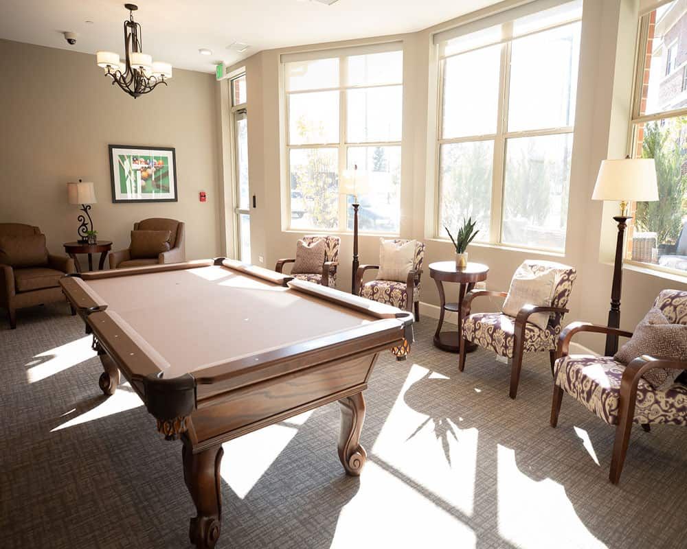 A sunlit billiard room with a pool table and cozy seating.