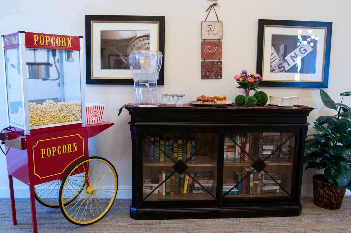 A cozy setup featuring a popcorn machine next to a cabinet with snacks, flowers, and decorative pictures on the wall.