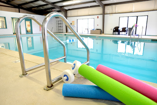 An inviting indoor swimming pool with colorful pool noodles and safety handrails.