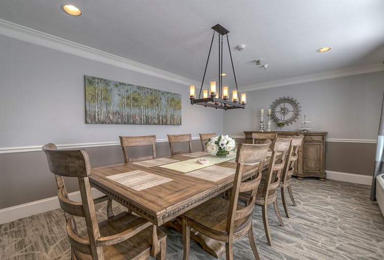 A modern dining room featuring a large wooden table, surrounded by chairs, and illuminated by a stylish chandelier.