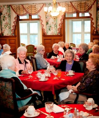 A group of seniors enjoying a social gathering at a dining table with red tablecloths.