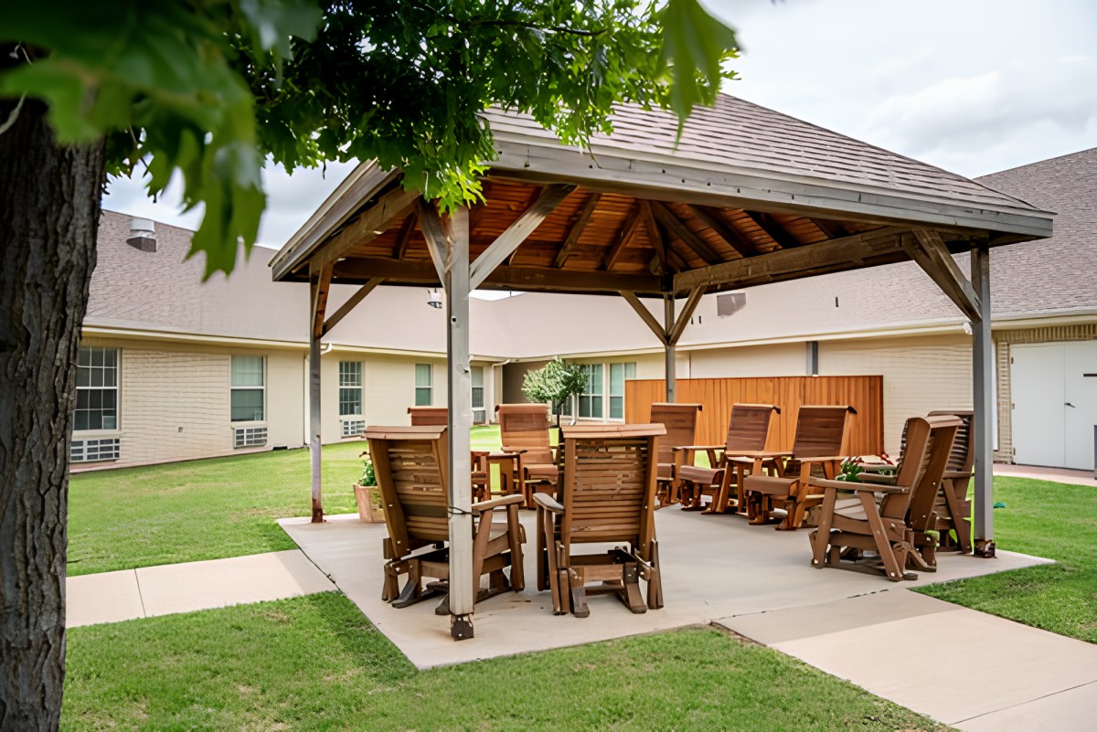 A cozy outdoor patio area with wooden gazebo and seating, set on a lush green lawn.