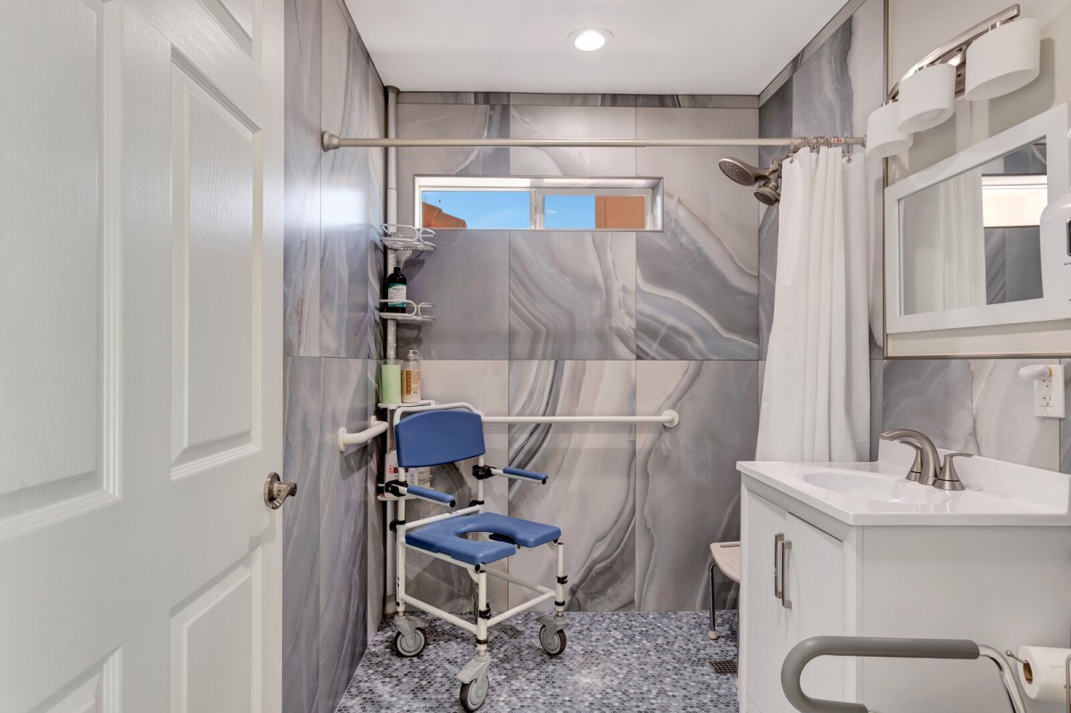 An accessible bathroom with a roll-in shower, featuring a wheelchair and grab bars.