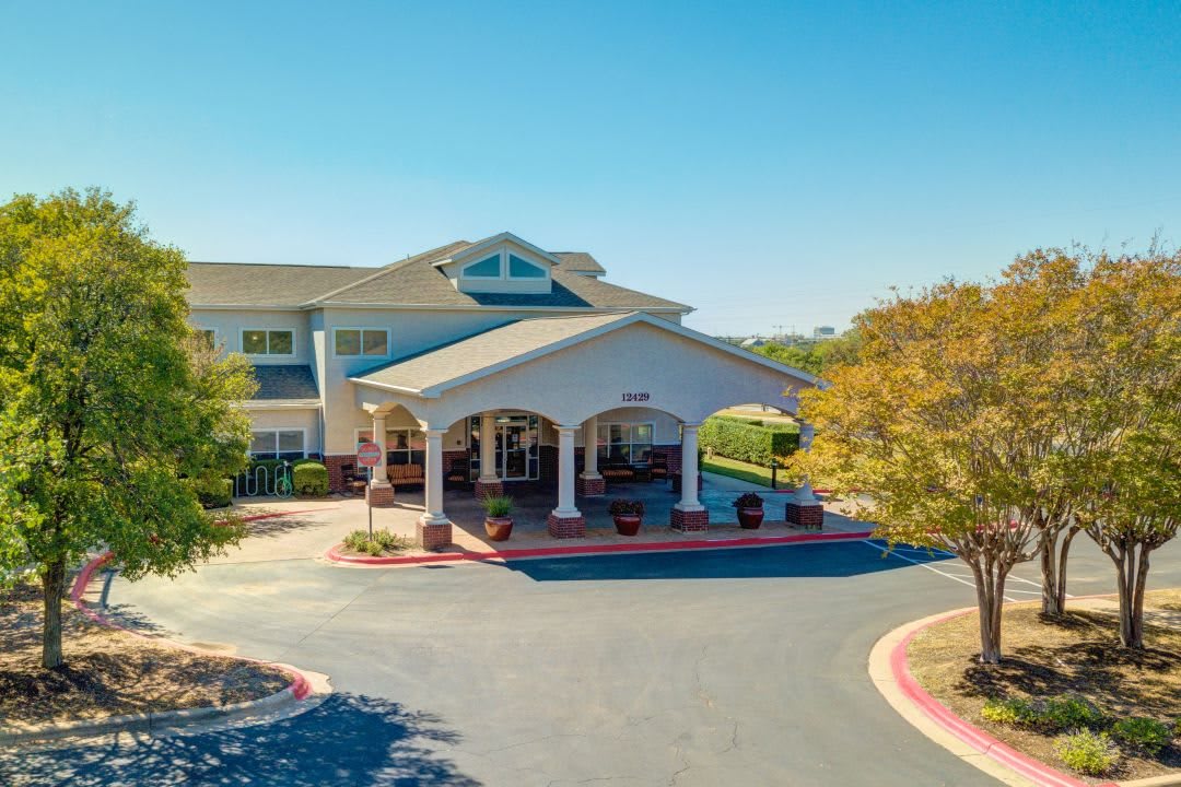 A sunny day view of a building entrance with a landscaped driveway and surrounding trees.