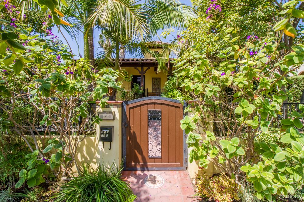 A tropical entrance to a house featuring lush greenery and a wooden gate.